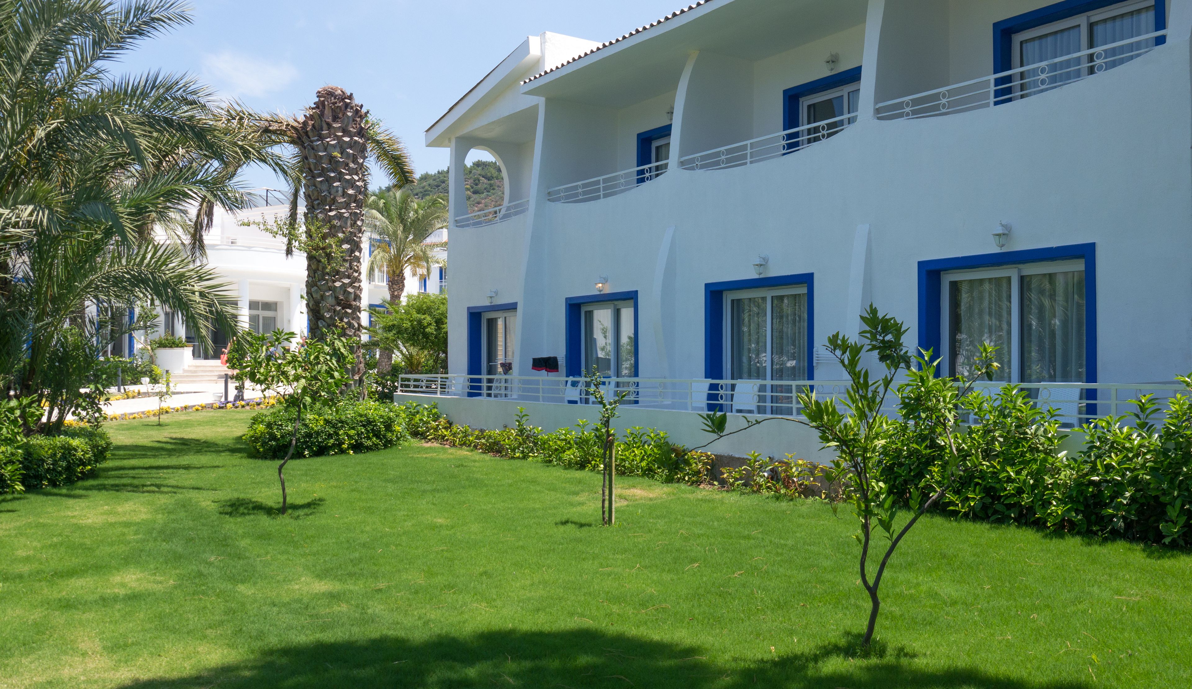 A hotel with a white exterior, blue accents, and a well-maintained lawn with palm trees.
