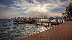 Une jetée en bois s’étendant sur des eaux calmes, sous un ciel dégagé, avec des montagnes lointaines à l’horizon.