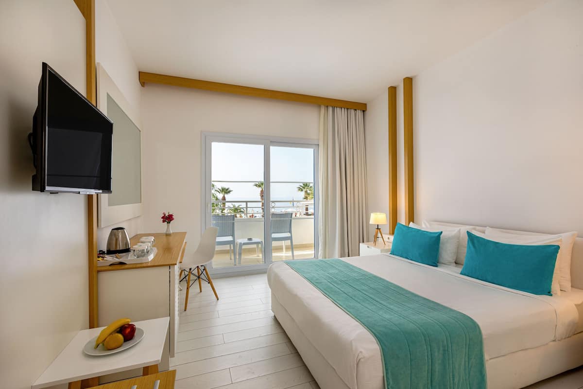 Ein Hotelzimmer mit Bett, Schreibtisch mit Stuhl, Fernseher und einem Balkon mit Meerblick.