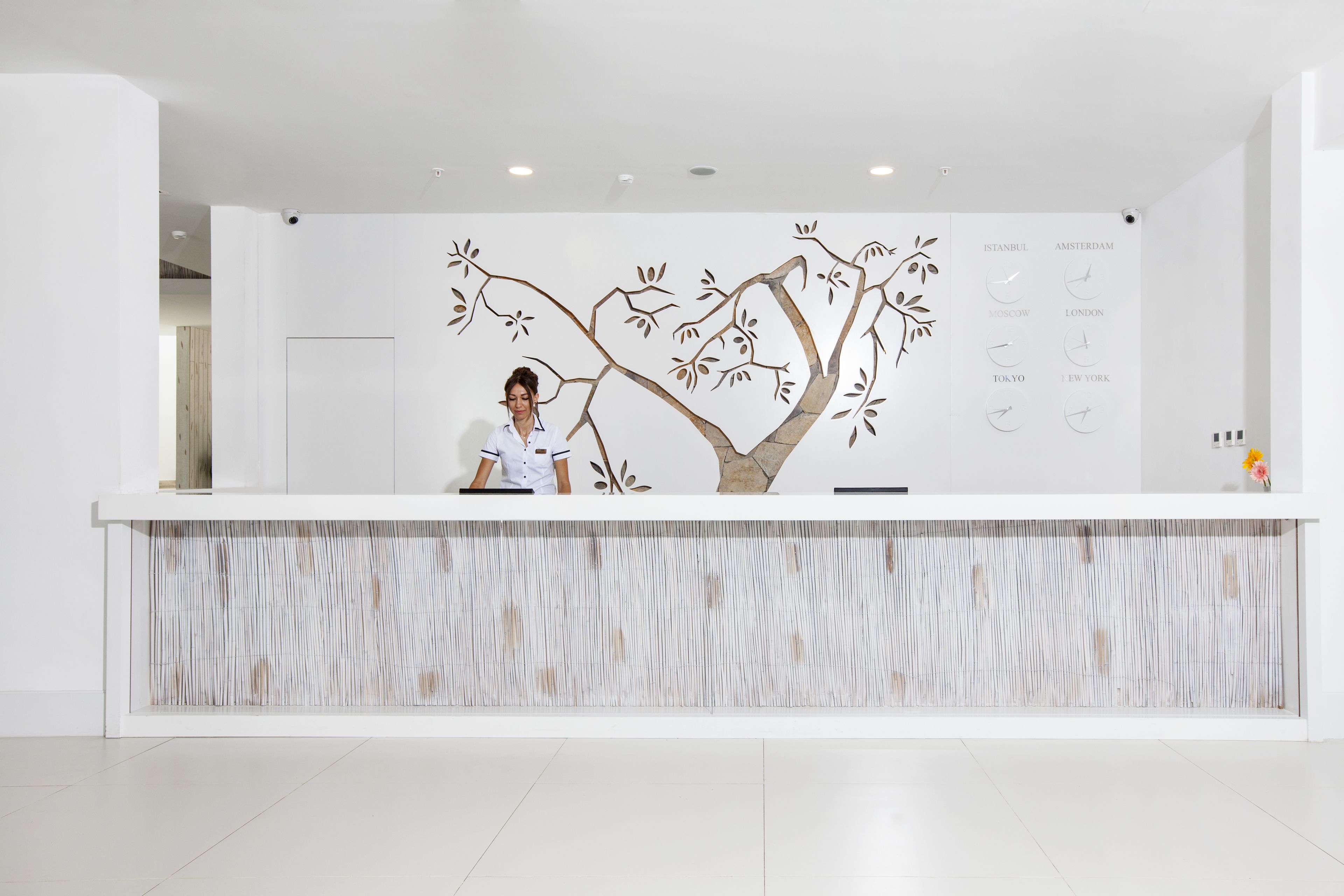 Un taulell de recepció de disseny modern, un mural amb un gran arbre i una llista de ciutats amb els seus rellotges corresponents.