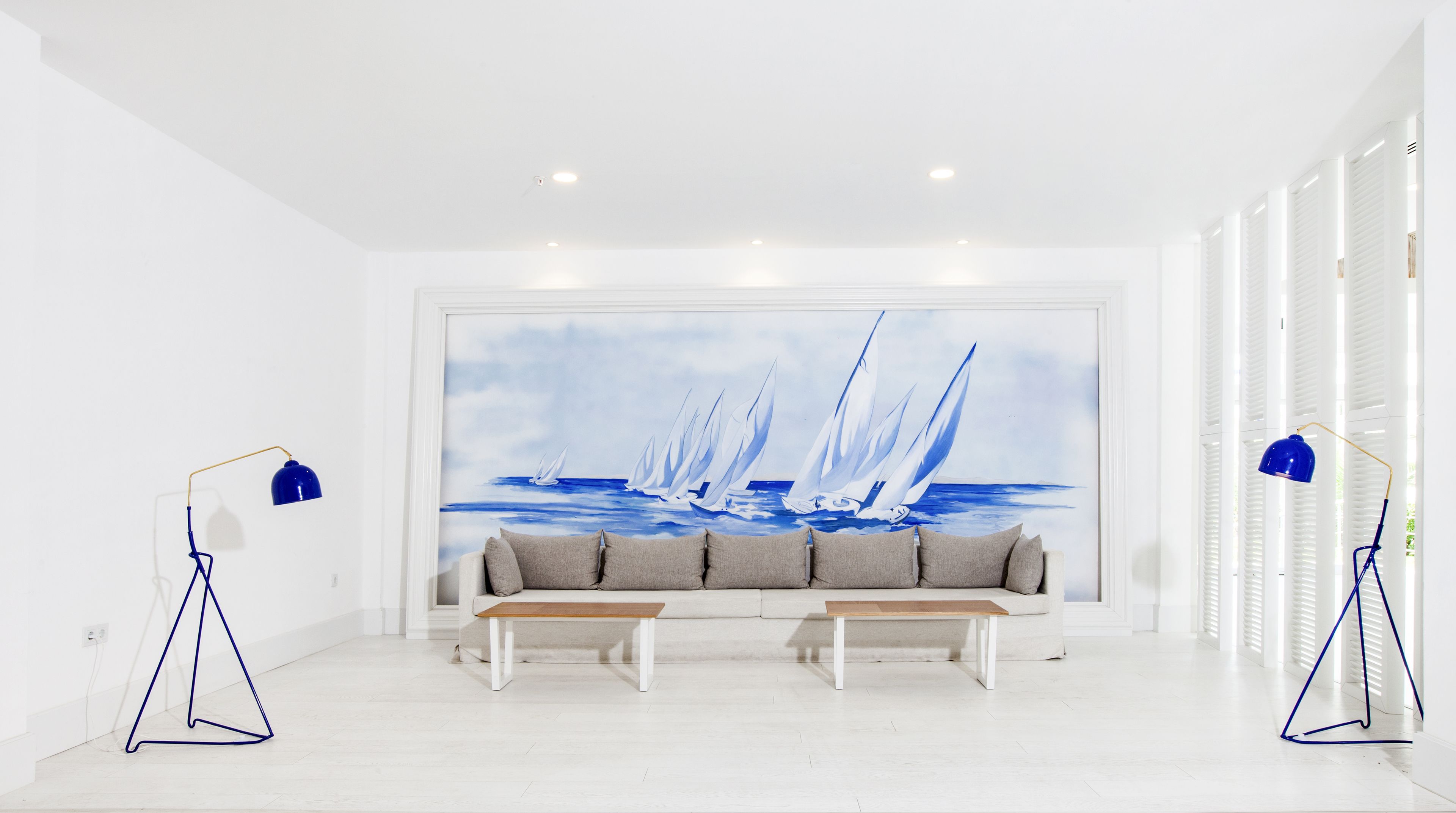 A modern living room with a large sailboat painting on the wall, a sofa, two side tables, and two floor lamps.