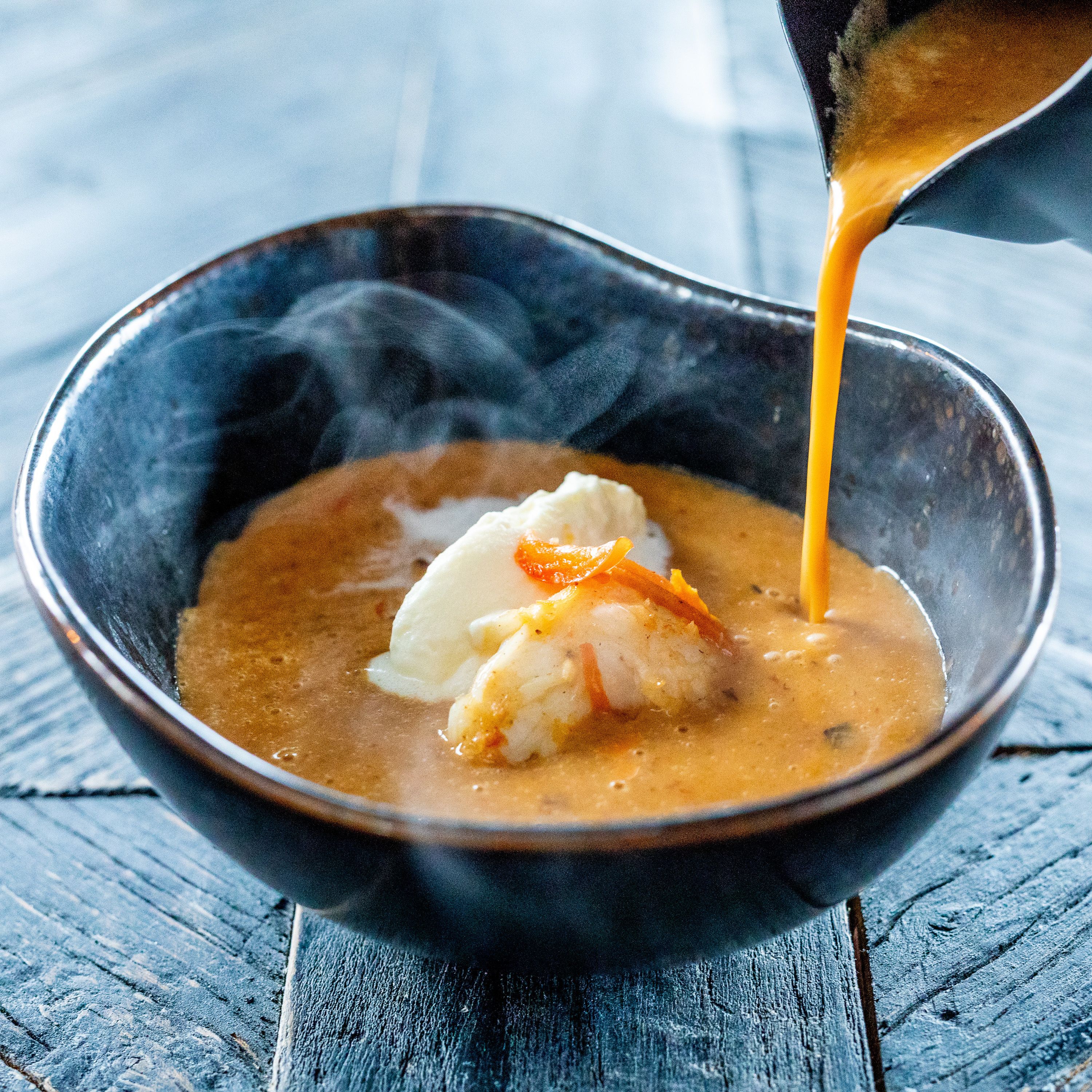 Un plato de sopa con salsa cremosa y un trozo de pescado, sirviéndose de una olla.