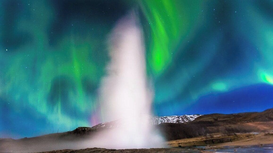 A geyser with a clear sky and aurora borealis in the background.