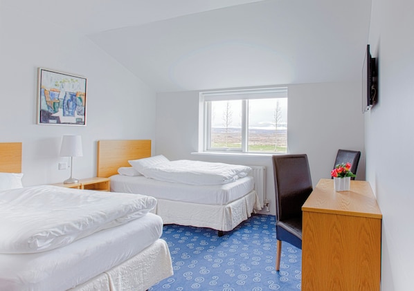 A hotel room with two beds, a desk with a chair, a TV, a window with a view, and a painting on the wall. - Litli Geysir (Bláskógabyggd)