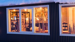 A modern building with large windows, interior lighting, and visible shelves with items. - Litli Geysir (Bláskógabyggd)