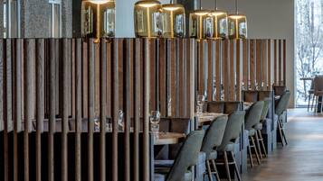 Un restaurante con separadores de madera, mesas, sillas e iluminación colgante.