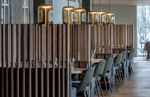Un restaurante con separadores de madera, mesas, sillas e iluminación colgante.