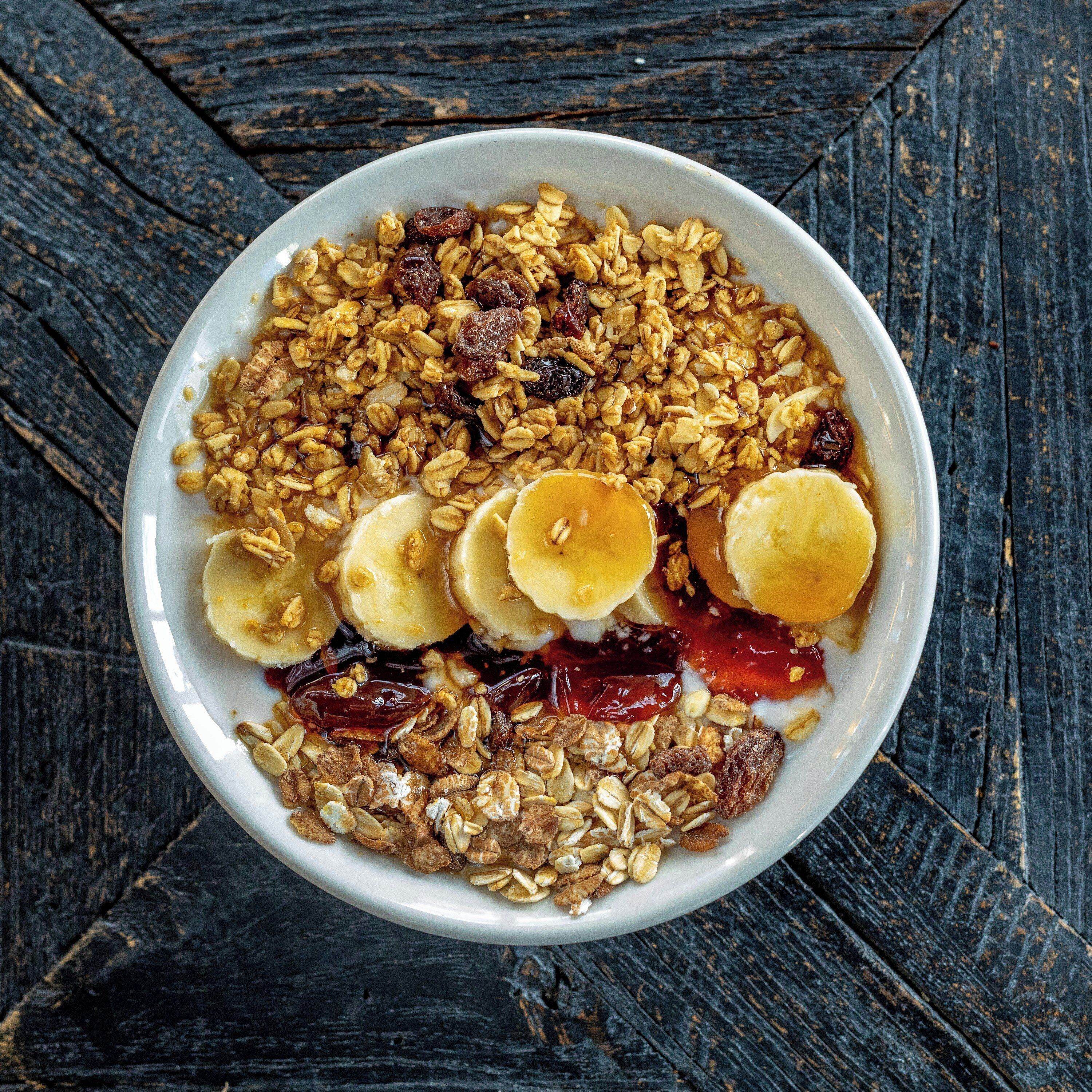 A bowl of cereal with bananas, raisins, and a liquid.