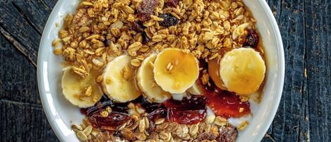 A bowl of cereal with bananas, raisins, and a liquid.