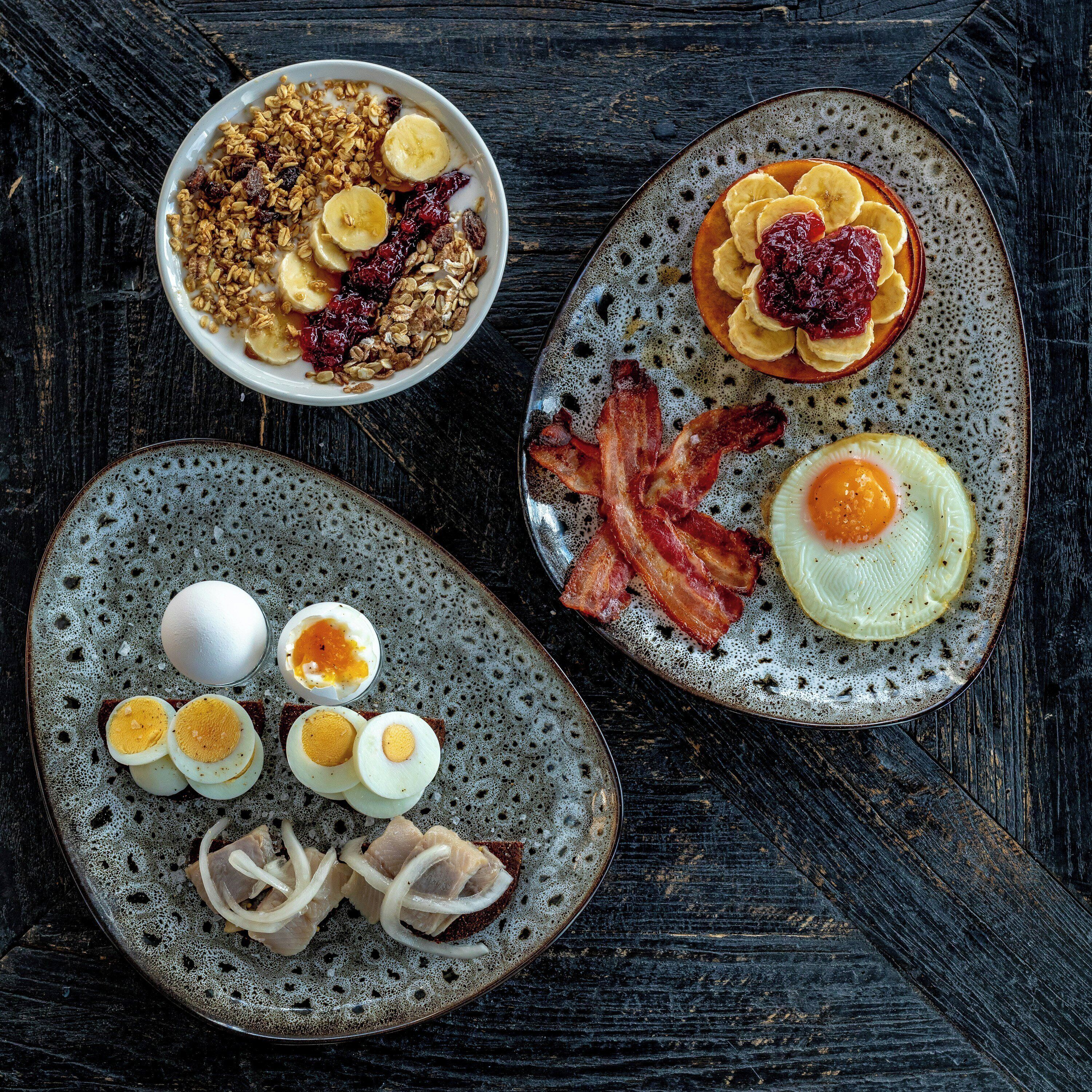 Un assortiment de mets pour le petit-déjeuner, servis sur des assiettes en céramique, comprenant des œufs, du bacon et des fruits.