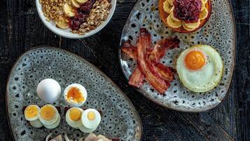Un assortiment de mets pour le petit-déjeuner, servis sur des assiettes en céramique, comprenant des œufs, du bacon et des fruits.