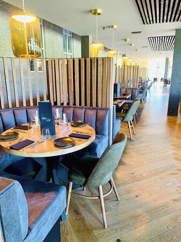 Un restaurante con mesas redondas, asientos tipo banca con cojines e iluminación colgante.