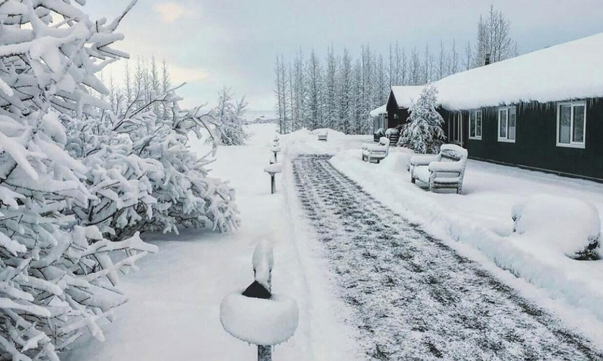 Un paisaje nevado con una casa, un camino y una silla.