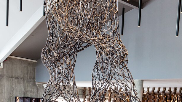 A modern interior with a unique metal sculpture centerpiece, wooden furniture, and a stone wall backdrop. - Litli Geysir (Bláskógabyggd)