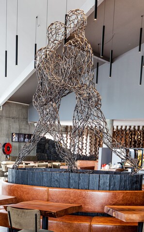 A modern interior with a unique metal sculpture centerpiece, wooden furniture, and a stone wall backdrop. - Litli Geysir (Bláskógabyggd)