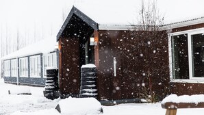 A wooden building with a sloped roof and large windows, surrounded by snow. - Litli Geysir (Bláskógabyggd)