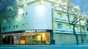 Un hotel de varios pisos con diseño moderno, que cuenta con un llamativo letrero de "URBANA SUITES" al nivel de la calle.