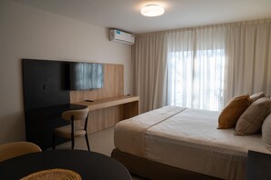 A hotel room with a bed, a desk, a chair, a television, and a window with curtains. - Urbana Suites (Mendoza)