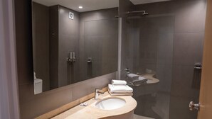 Un baño moderno con un lavamanos curvo, cabina de ducha con mampara de vidrio y un espejo grande.