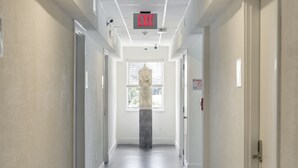 A hallway with a marble statue, an exit sign, and a window with blinds. - Treehouse  Hotel (Miami)