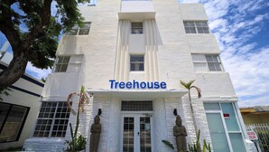 A building with a sign reading "Treehouse" at the entrance, featuring a white facade, large windows, and a gated driveway. - Treehouse  Hotel (Miami)