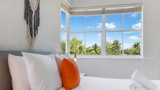 A hotel room with a bed, pillows, a window with a view of trees, and a macrame wall hanging. - Treehouse  Hotel (Miami)