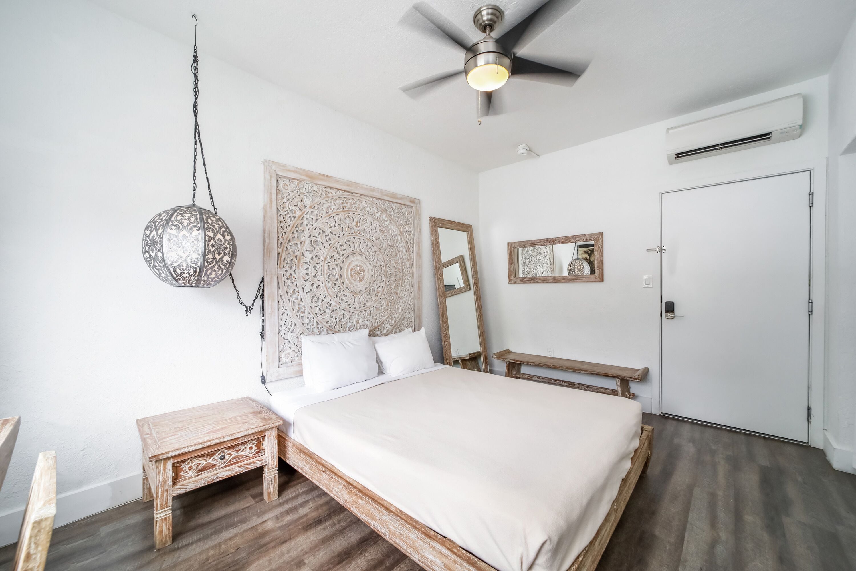 Une chambre à coucher comprenant un lit, un ventilateur de plafond, un luminaire suspendu, une table de chevet, un miroir et un appareil de climatisation.