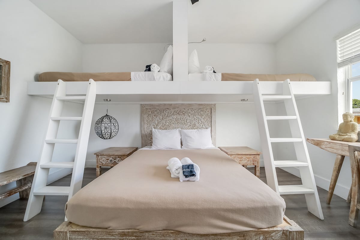 A bunk bed with a ladder, a bedside table, and a hanging light fixture.