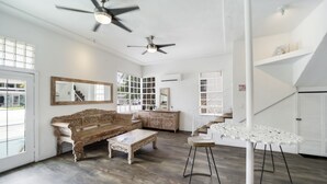 A spacious living area with a wooden bench, a coffee table, and a white bar stool. There are two ceiling fans, a large mirror, and a staircase leading to an upper level. - Treehouse  Hotel (Miami)