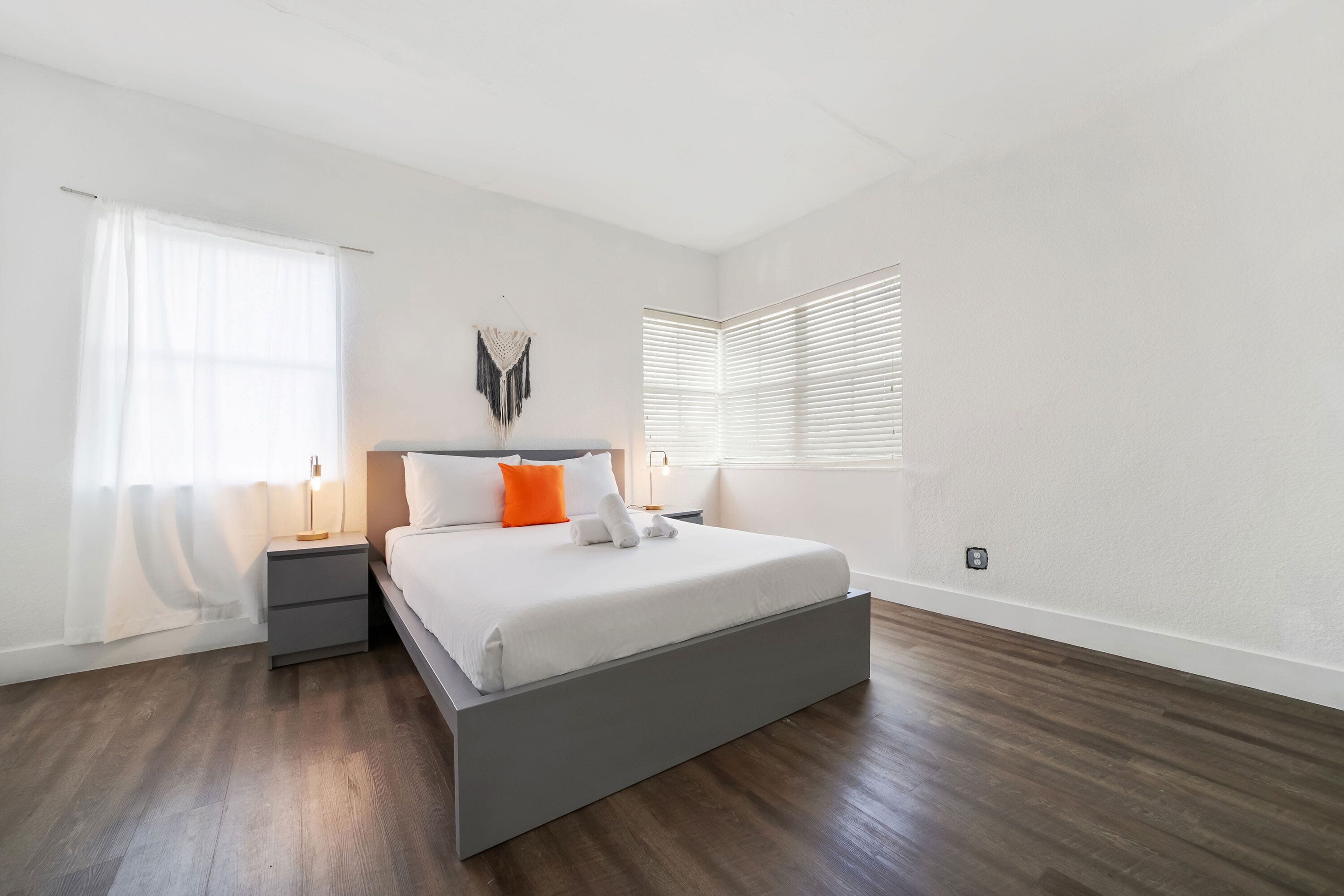 A modern bedroom with a bed, bedside tables, a wall-mounted light, and a window with blinds.