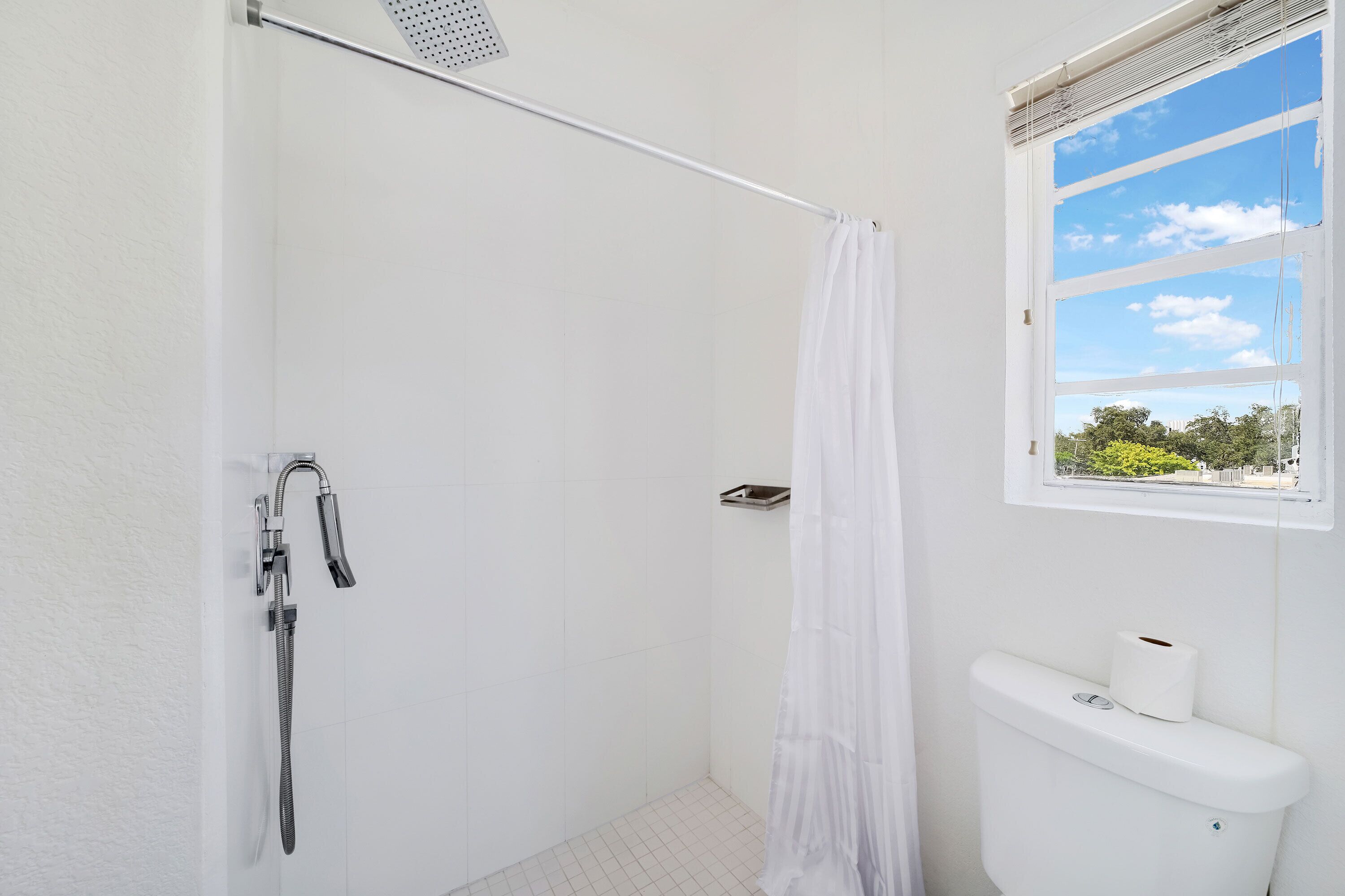 Une salle de bain avec douche, toilettes et fenêtre.
