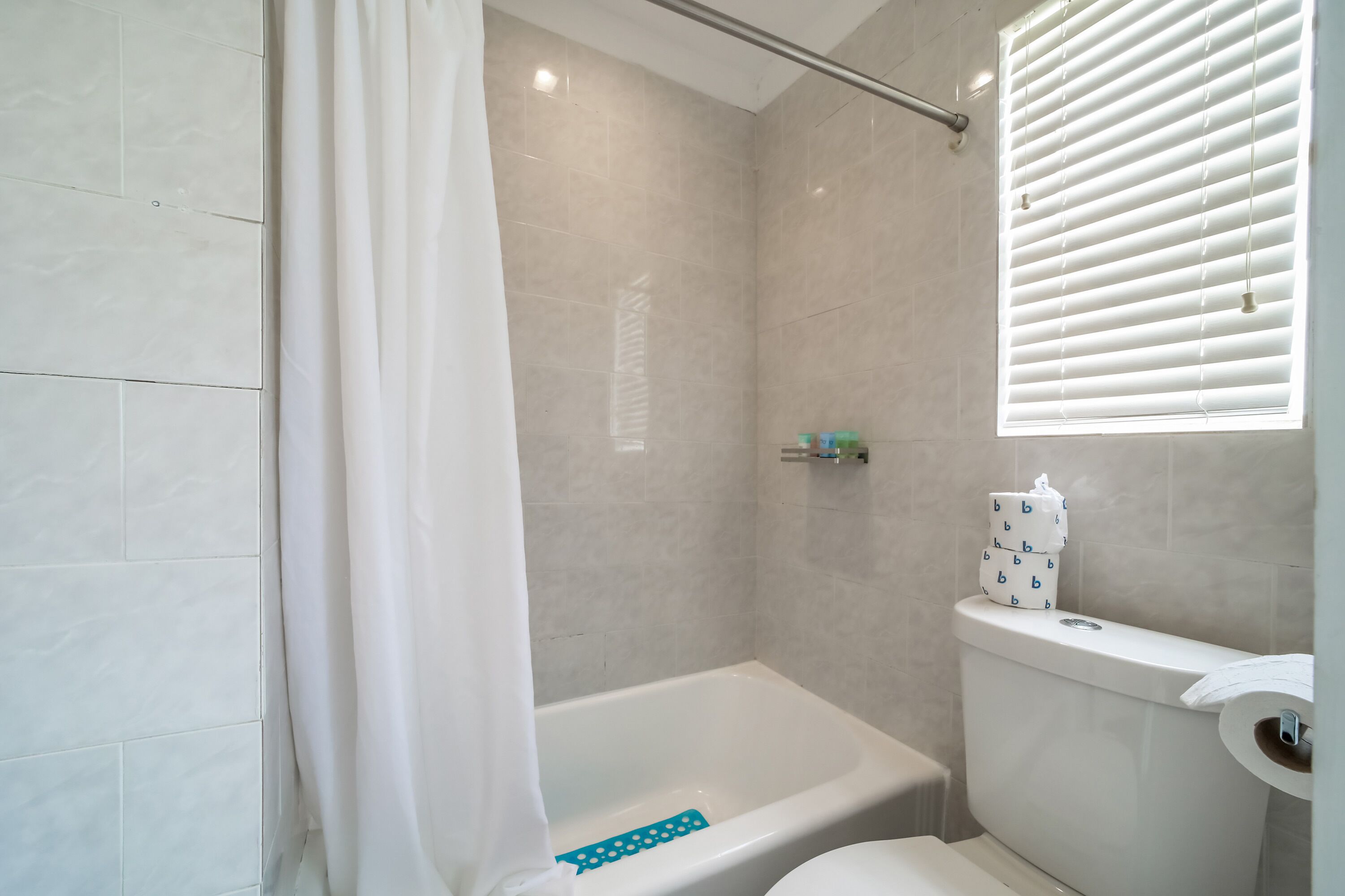 A bathroom with a bathtub, toilet, and window with blinds.