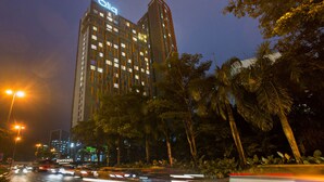 A high-rise hotel with a prominent "Qia" sign at the top, surrounded by lush greenery and palm trees. - Qliq Damansara (Petaling Jaya)