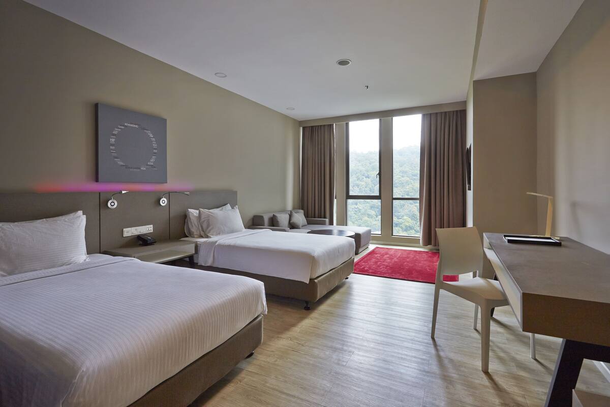 A hotel room with two beds, a desk, a chair, a red rug, and a large window with curtains.