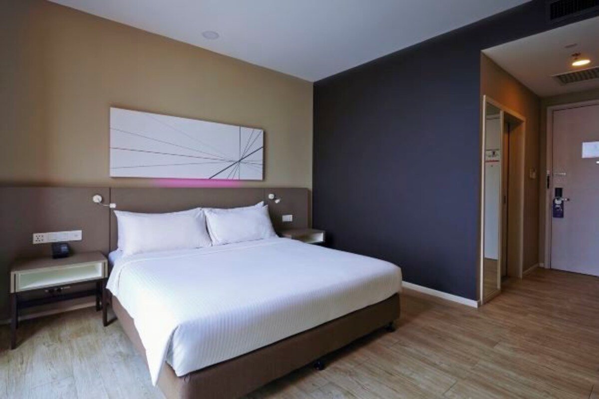 A modern hotel room with a large bed, bedside tables, and a wall-mounted artwork.
