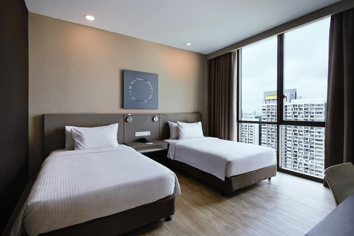 A hotel room with two beds, a nightstand, a wall-mounted clock, and a large window with a city view.