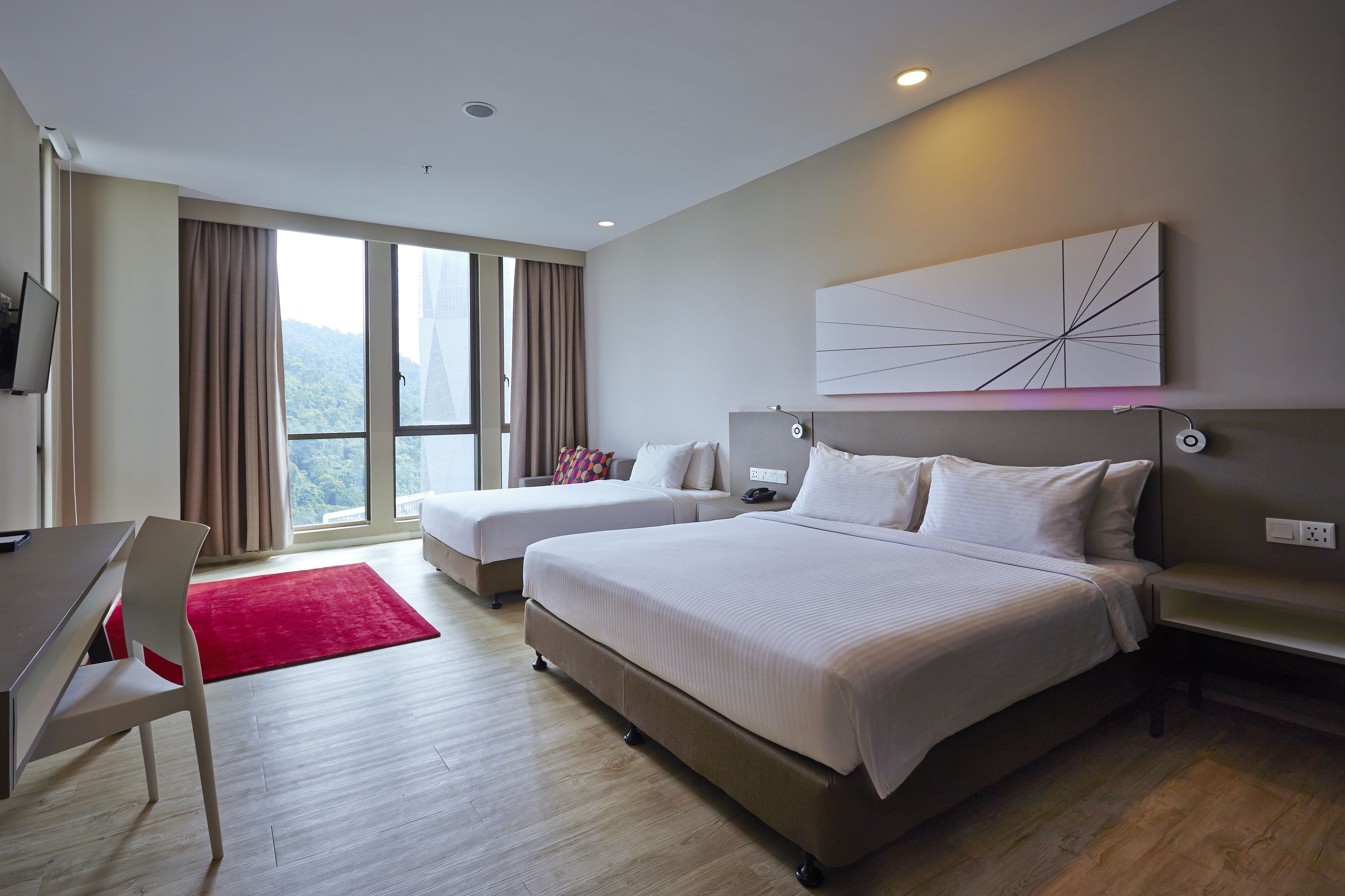 A hotel room with a large bed, a desk, a chair, and a red rug.