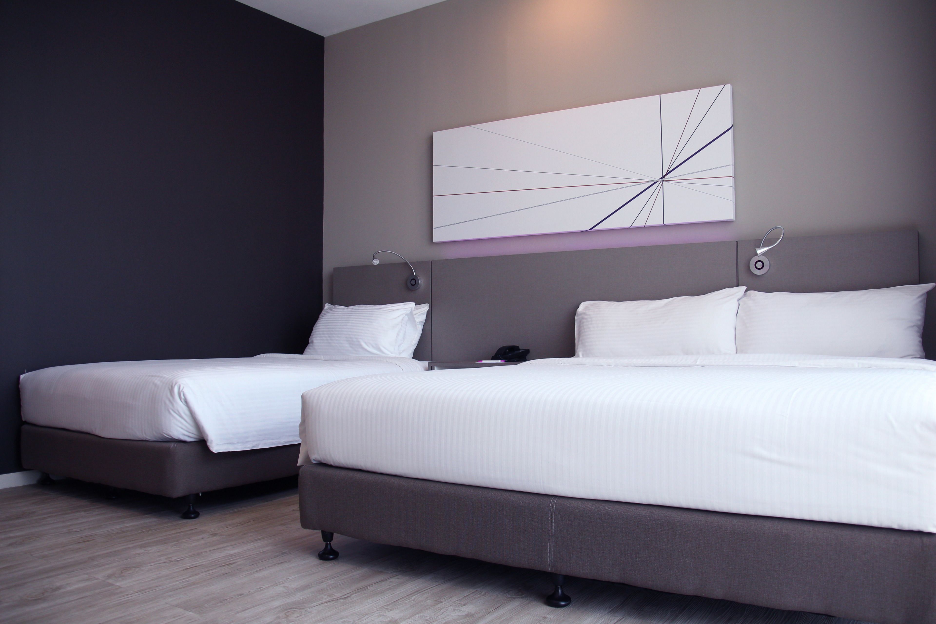 A modern hotel room with two beds, a large abstract painting, and a bedside table with a lamp.