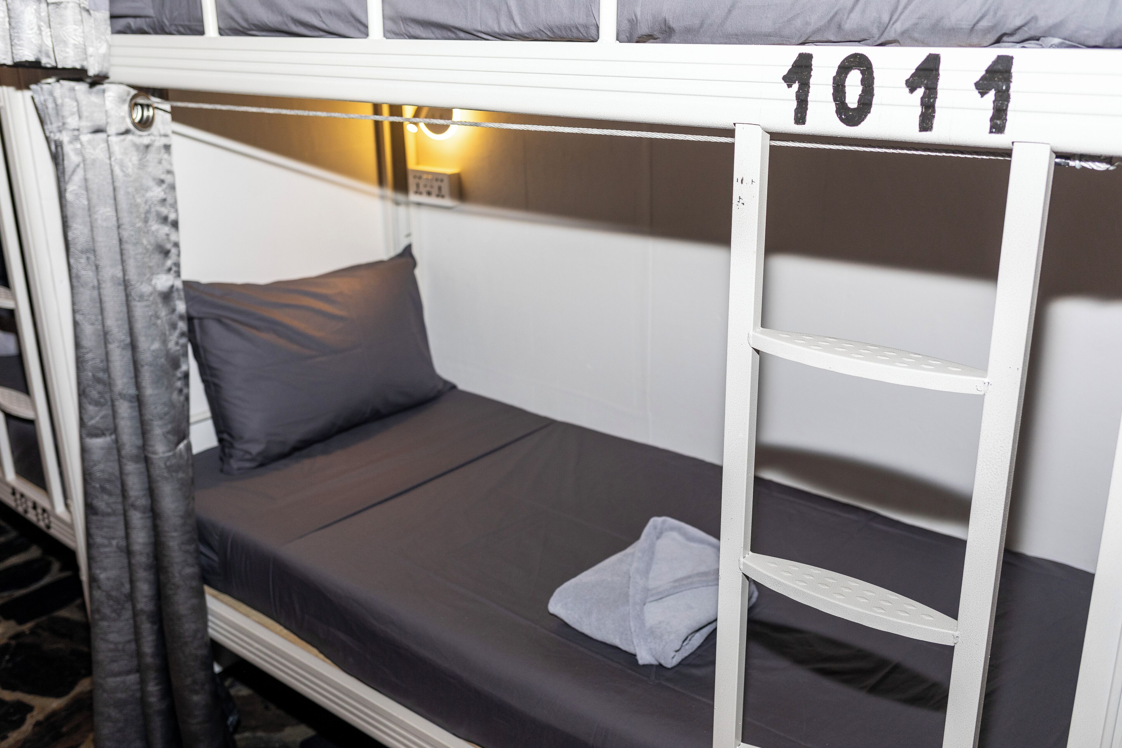 A bunk bed with a number '1011' on the headboard, a grey pillow, and a folded towel on the lower bunk.