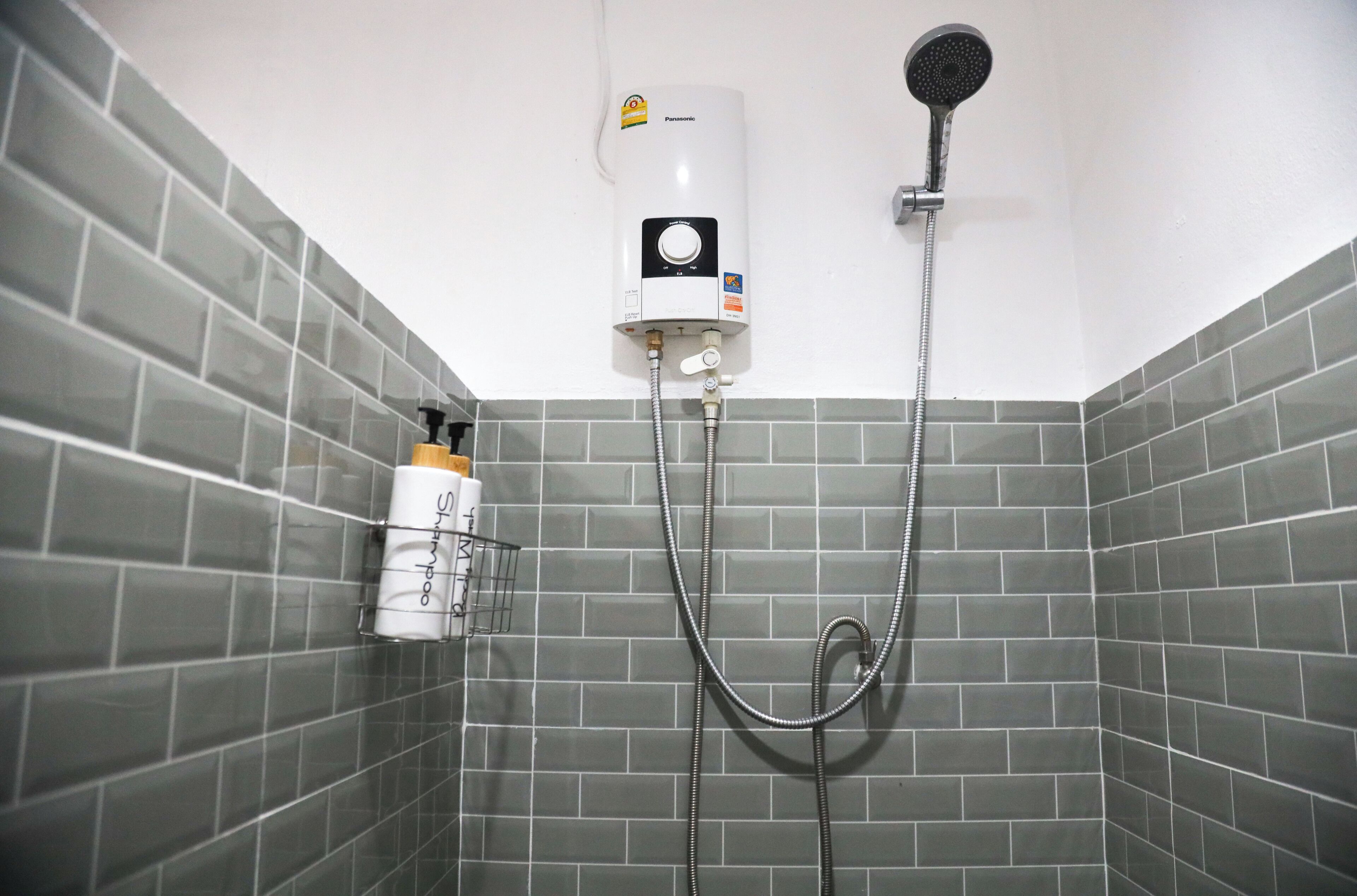Baño con pared de ducha en tono gris, calentador de agua blanco y cabezal de ducha.