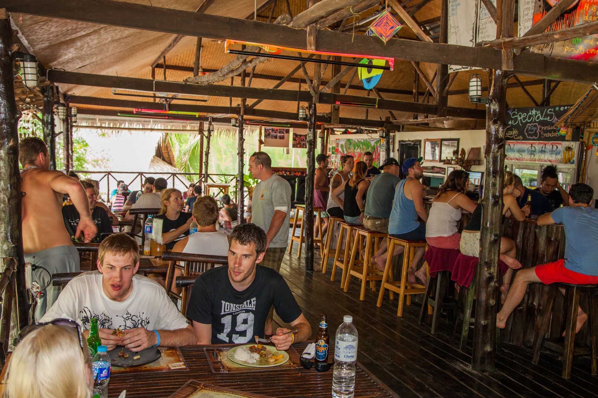 A crowded indoor dining area with wooden tables and chairs, a high ceiling with exposed beams, and a rustic ambiance.