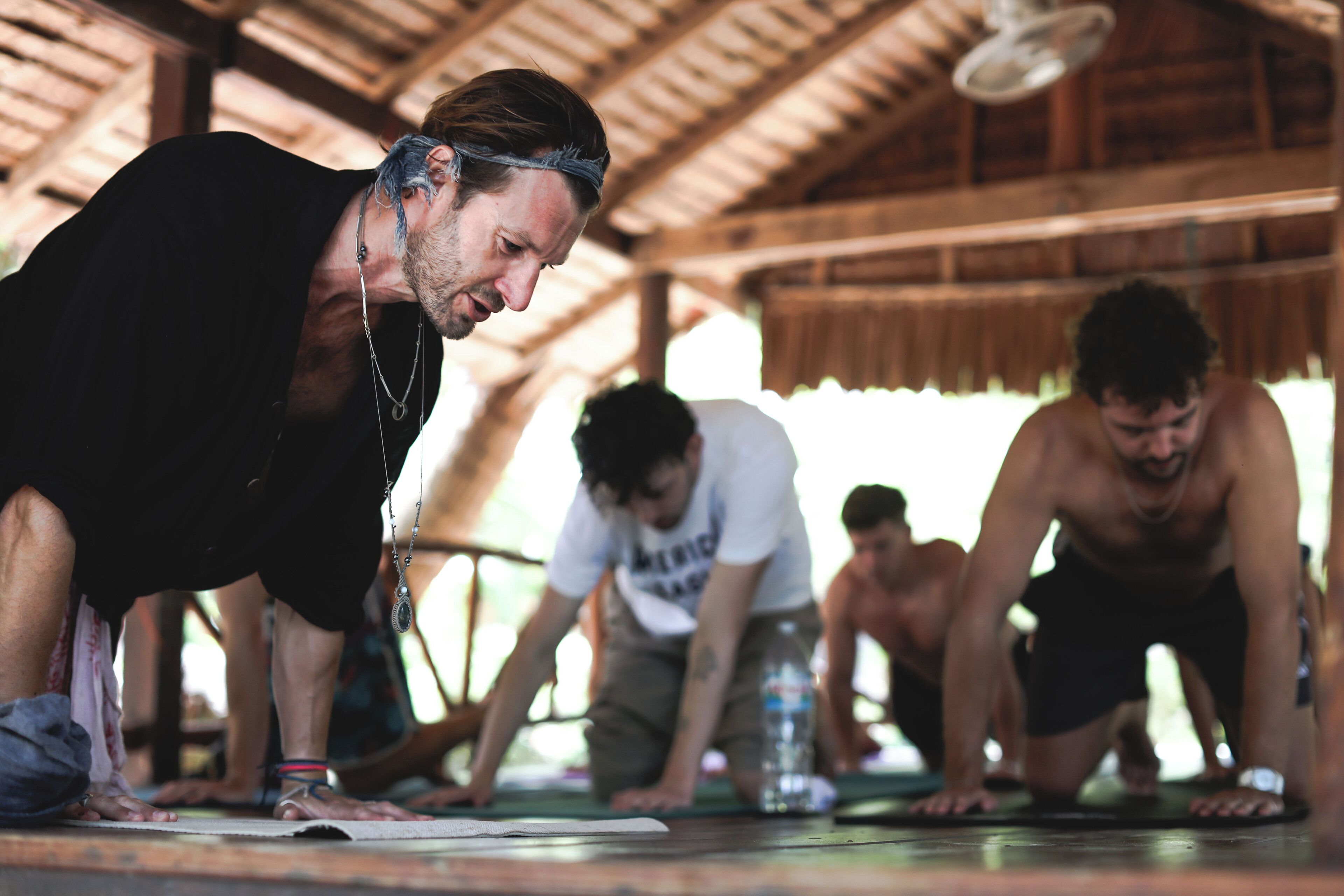 Un grupo de personas en un espacio exterior cubierto, posiblemente un gimnasio o centro de acondicionamiento físico, con una estructura de madera en el techo.