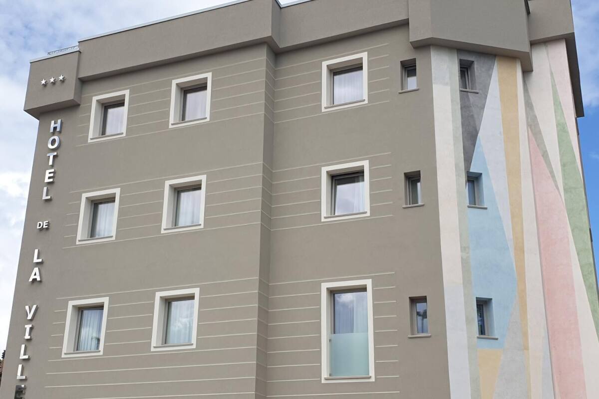 A multi-story hotel building with a modern facade, featuring a series of windows and a distinctive vertical design element on the right side.