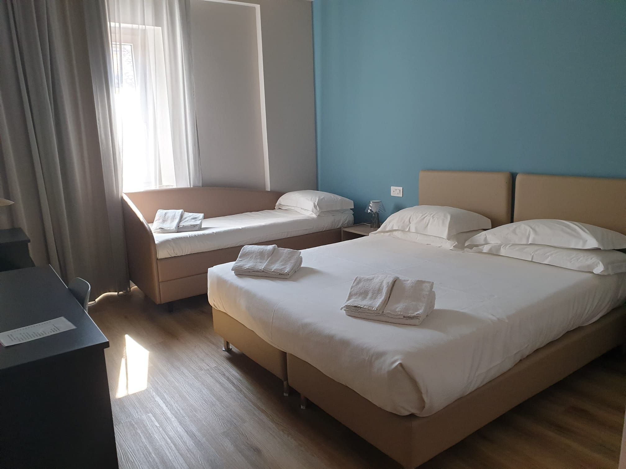 A hotel room with two beds, a desk, and a window with curtains.
