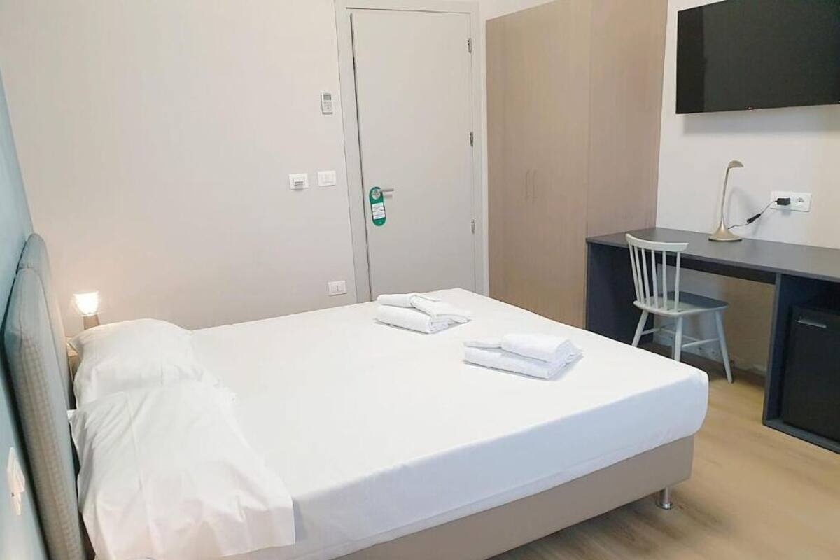 A hotel room with a bed, a desk, a chair, and a TV mounted on the wall.