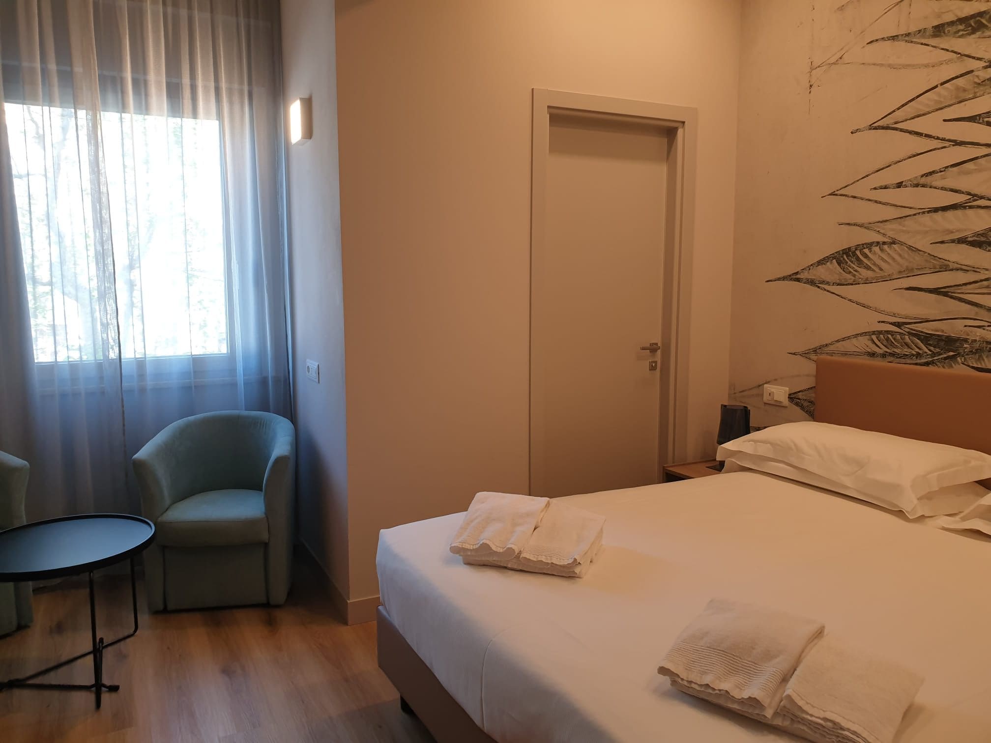 A hotel room with a bed, a chair, a table, and a door.