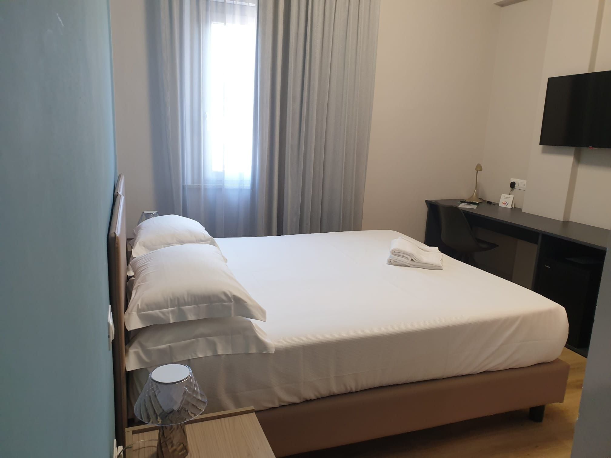 A hotel room with a bed, a desk, a TV, and a window with curtains.