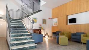 A modern interior with a marble staircase, wooden panel walls, and a seating area with colorful sofas. - Hotel De La Ville (Fano)