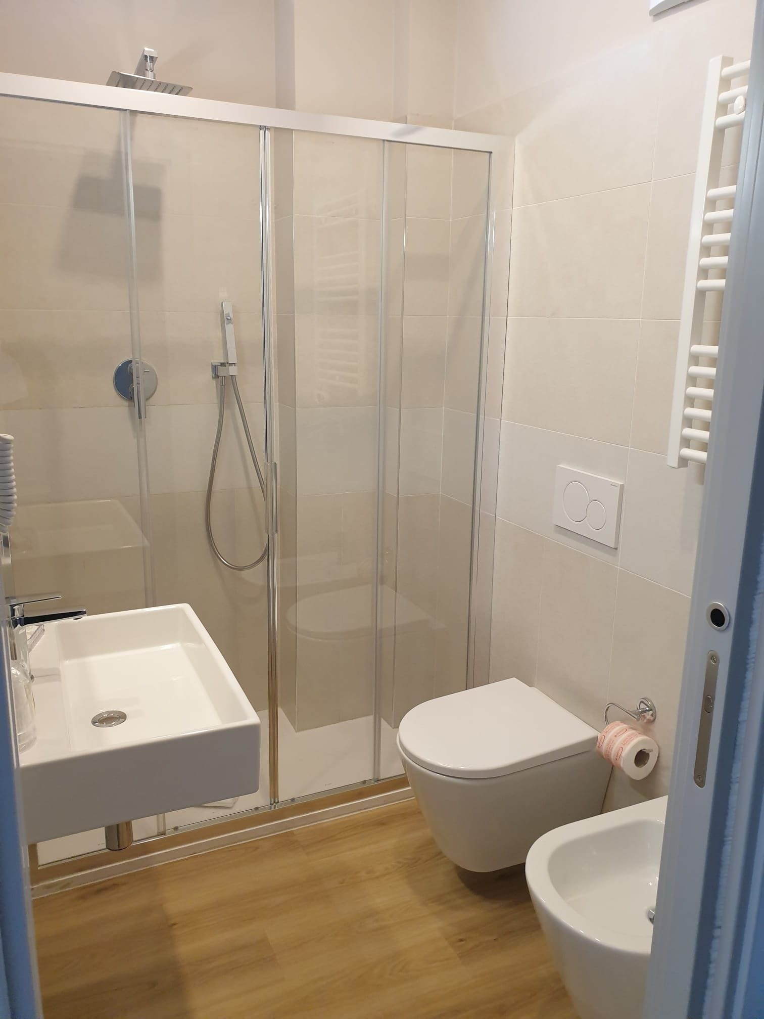 A bathroom with a glass-enclosed shower, a white sink, a toilet, and a towel rack.