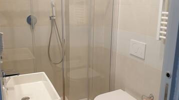 A bathroom with a glass-enclosed shower, a white sink, a toilet, and a towel rack.